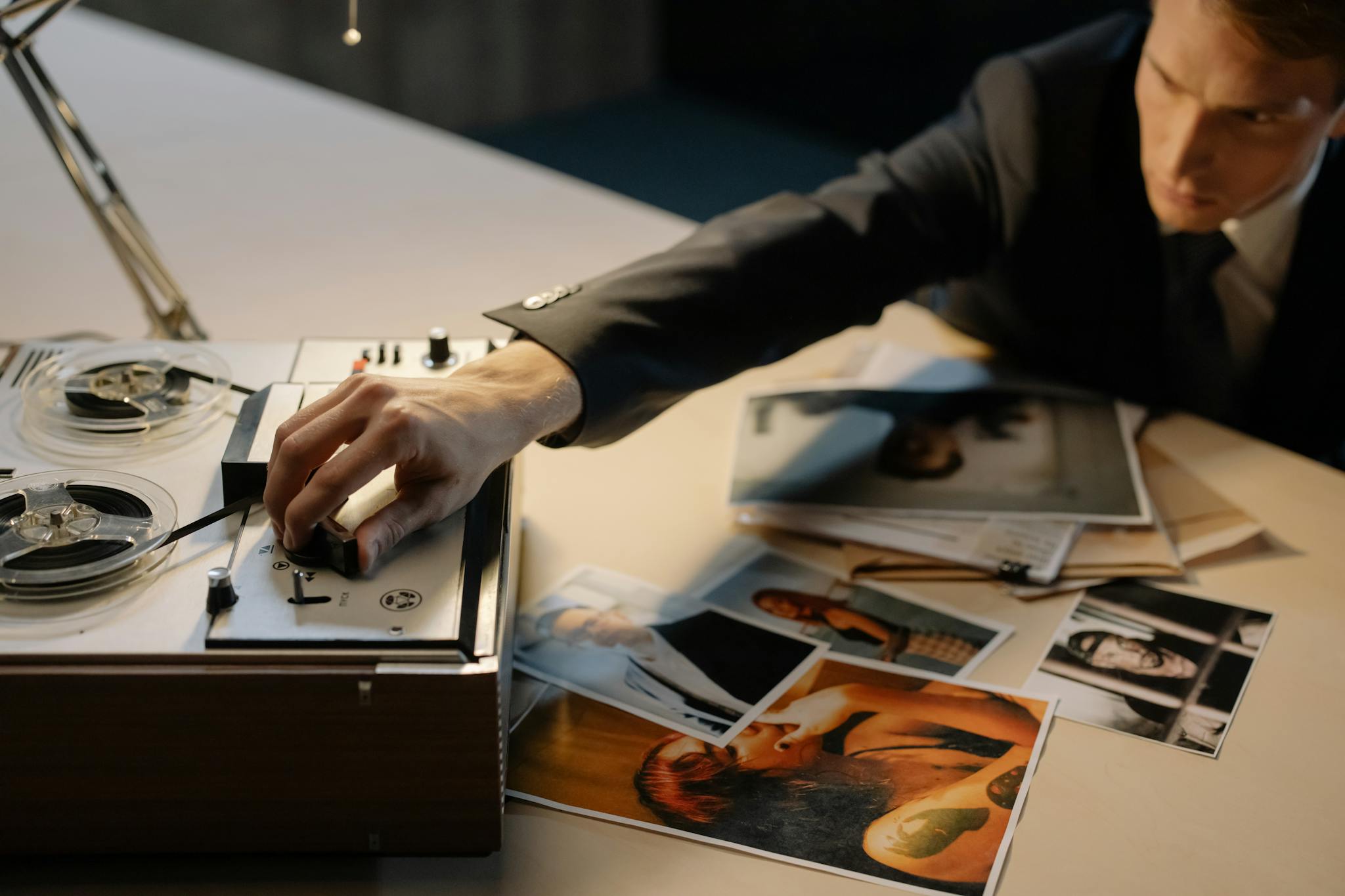 A detective adjusting a tape recorder during an investigation with photos spread on a table.
