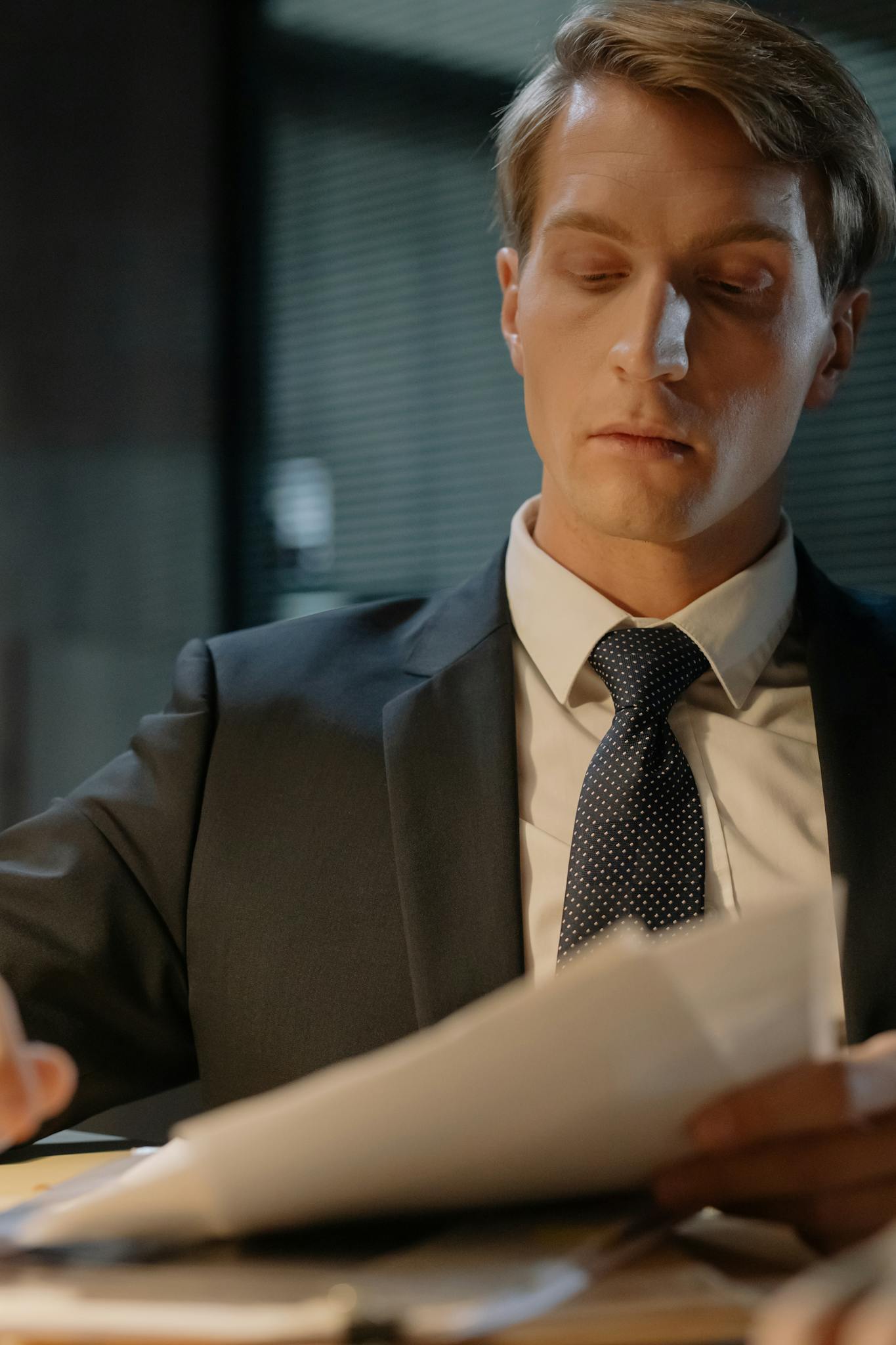 A focused detective examining papers at a desk in an office setting.